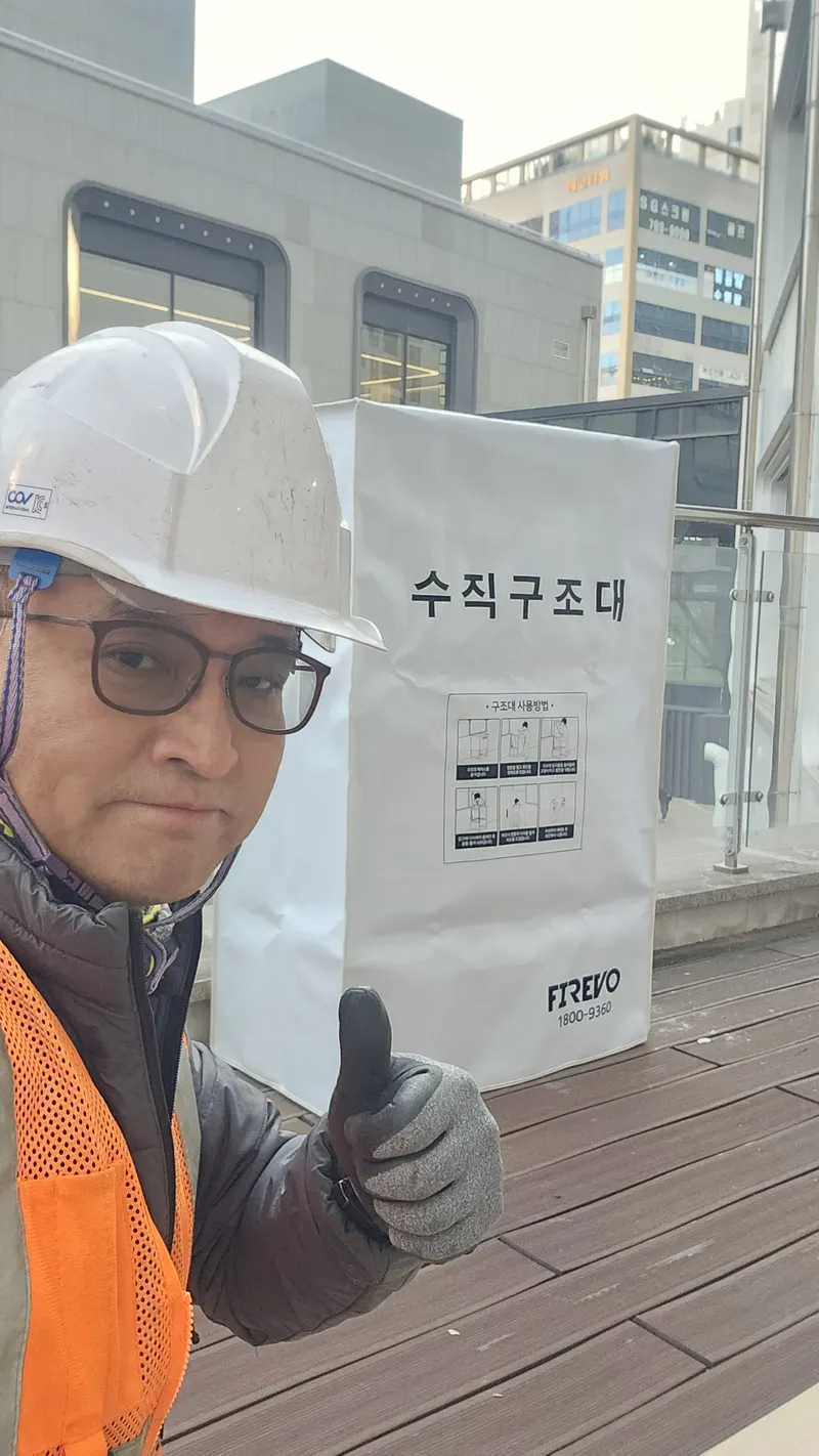 빌딩 비상탈출기구 안내 — 작업자가 수직구조대 설치 현장에서 상태를 확인하는 모습
